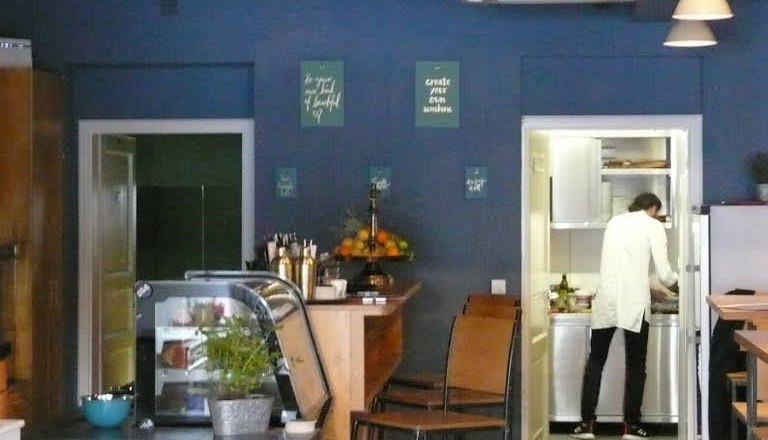 the counter, © Süd - das Kulturcafé Interior view of a café with blue wall, counter, bar stools and a person in the kitchen.