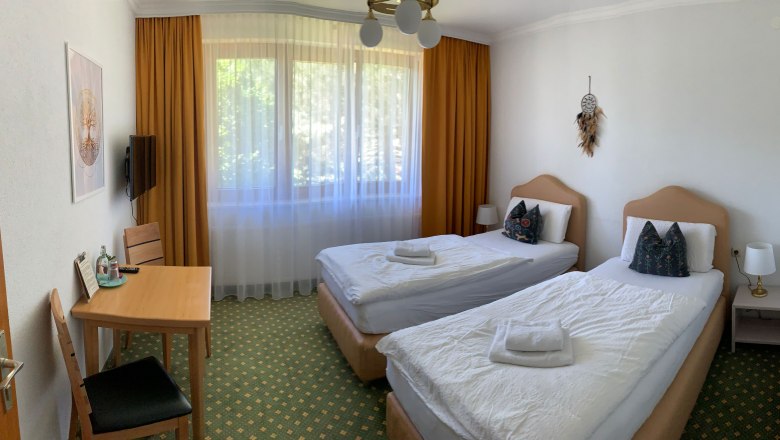 Double room single beds, © Dorfschmiede eG A hotel room with two single beds, a table with chairs and a window with curtains.