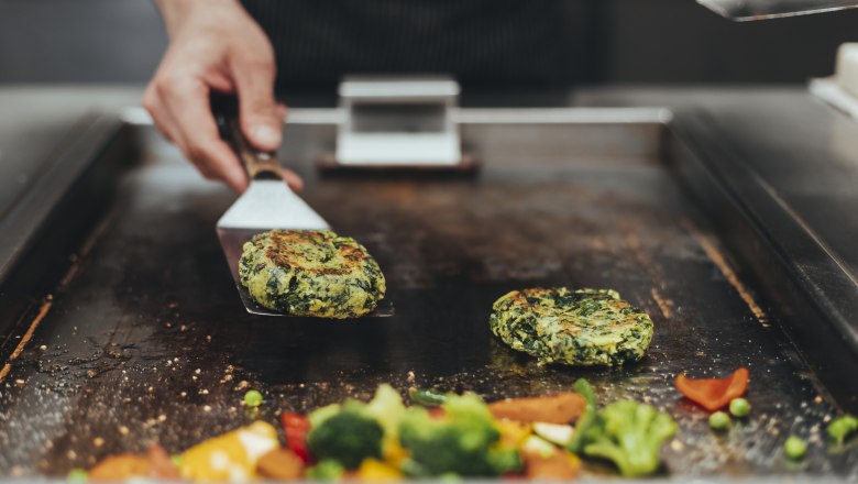 Colorful cuisine with own vegetable and herb cultivation, © Niederösterreich Werbung/David Schreiber A cook turns vegetable patties on a grill plate, surrounded by colorful vegetables.