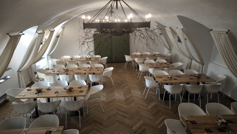 Hall of Arms in the Freiherr, © Markus Jokesz Elegant hall with wooden tables, parquet floor, white chairs and iron chandelier.