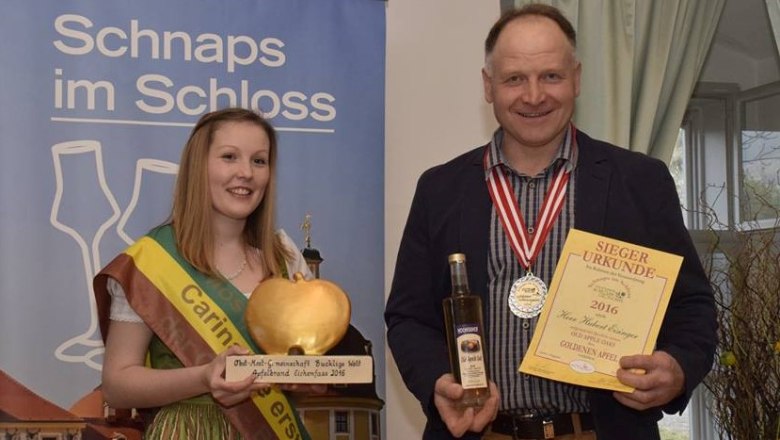 Variety winner apple in oak barrel, © Sinawehl Waltraud Two people hold a trophy and a certificate at an awards ceremony.
