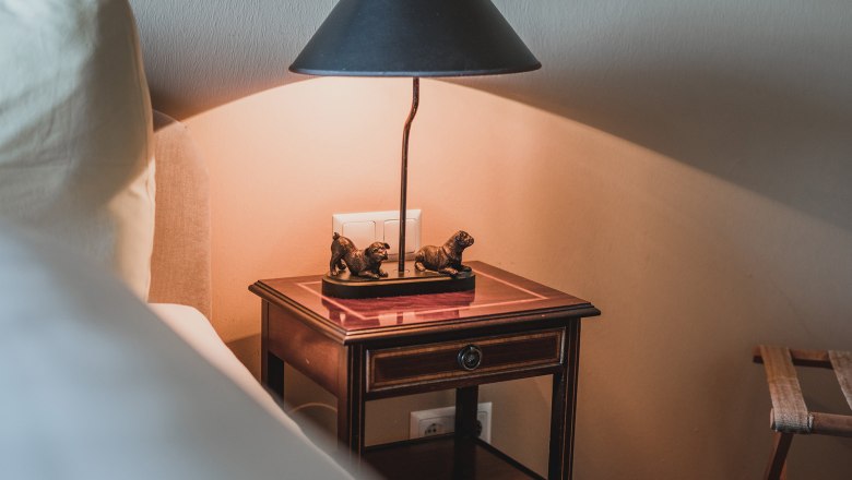 Double room with castle view, © Schlossschenke Bedside table with lamp and dog sculptures in a double room.