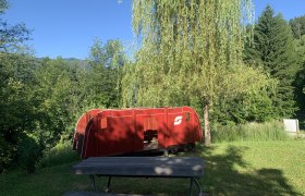 Wooden locomotive, © TVB Semmering-Rax-Schneeberg Red toy locomotive outdoors next to a tree and a wooden bench.