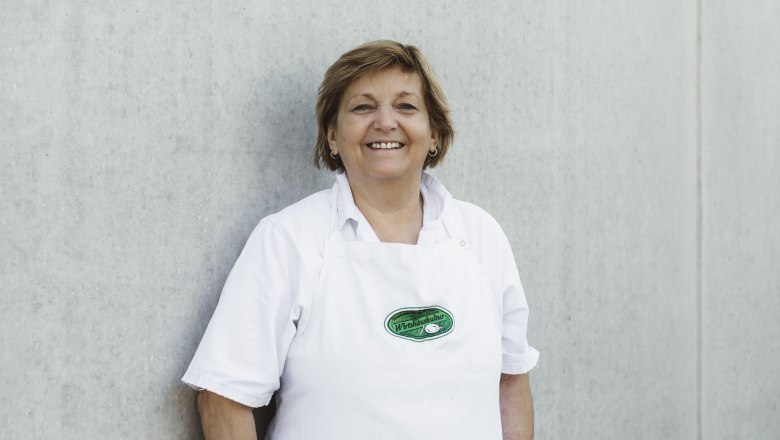Hermine Kerschbaummayr, © Niederösterreich Werbung/David Schreiber Woman in a white apron in front of a gray wall.