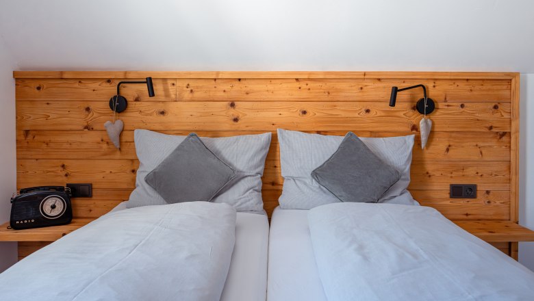 Leopold an der Ybbs, © © Niederösterreich Werbung/ Maximilian Pawlikowsky Comfortable double bed with wooden back panel, gray cushions and blankets. A retro radio on the left, a reading lamp and heart decoration on the right.