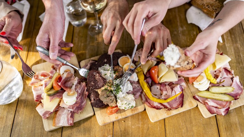 Heurigen snack, © Weinviertel Tourismus GmbH / Herbst Several hands reach for cold cuts and cheese on wooden platters.
