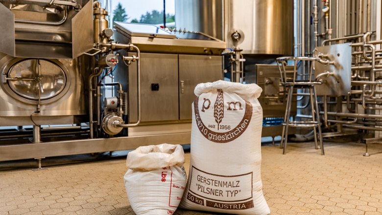 Schwarzbräu - Brewery, © Wiener Alpen, Christian Kremsl Bags of barley malt in a brewery in front of stainless steel machines.