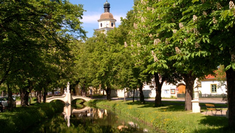 Municipality of Straß im Straßertale, © Gemeinde Straß im Straßertale An idyllic park with a small river, a bridge and a church tower in the background.