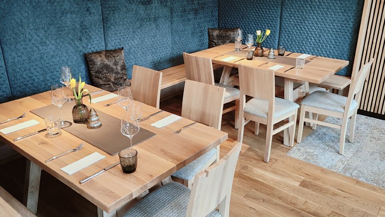 Guest area, © das GrimmenStein Modern restaurant with covered wooden tables, chairs, blue upholstered walls, wooden elements and decorations.