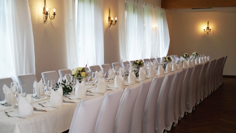 Event hall, © Schlossschenke Elegant function room with long, festively laid tables and white chairs.