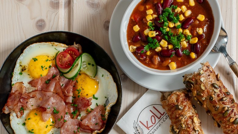 Hot snacks, © Koll GmbH Various hot snacks on a table, including fried eggs with bacon, sandwiches and a bowl of chili.