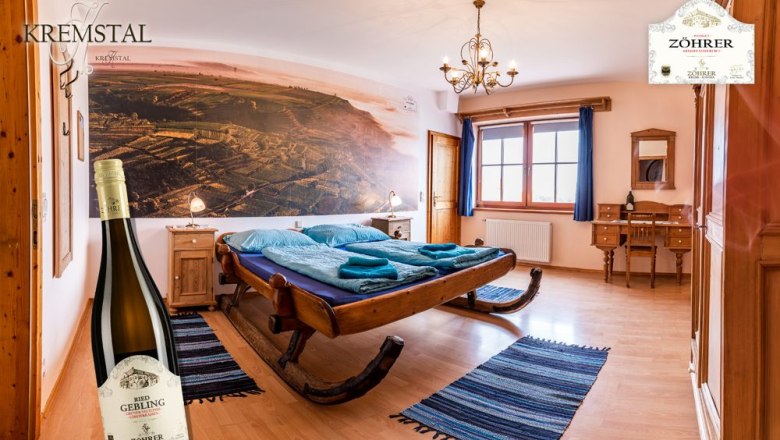 Room no. 6 Sleigh bed, © Weingut Zöhrer Cozy room with sleigh bed, wooden furniture and large mural. A bottle of wine stands in the foreground.