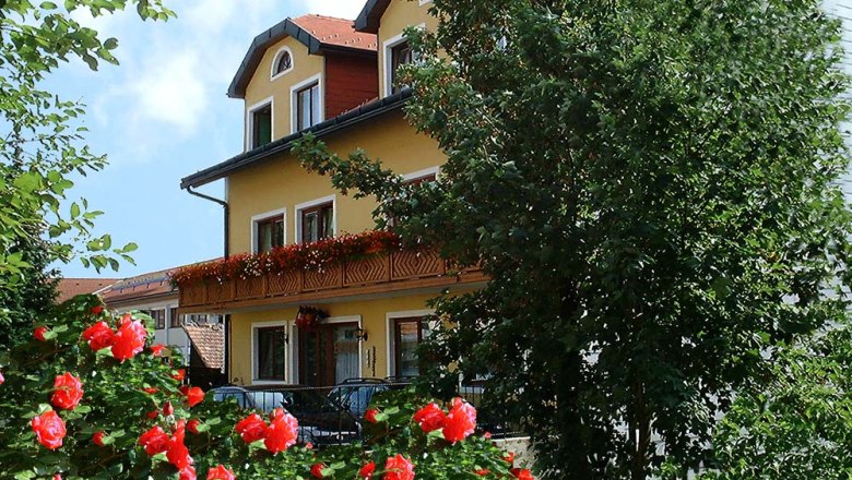 Hotel Rosner, © Hotel Rosner Yellow hotel building with balcony, surrounded by blooming red roses and trees.