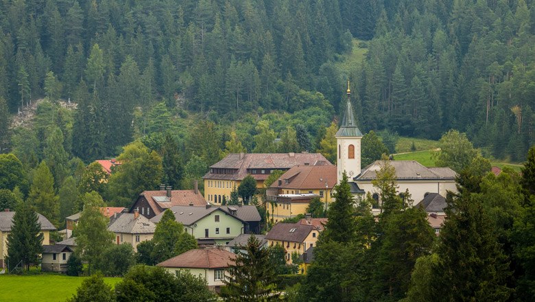 View of Rohr im Gebirge, © Wiener Alpen, Christian Kremsl A village with a church surrounded by wooded mountains.