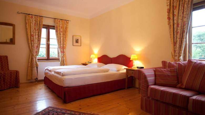 Bedroom 2, © Renaissancehotel “ Raffelsberger Hof “ Cozy bedroom with double bed, red headboard, striped sofa and curtains, wooden floor and carpet.