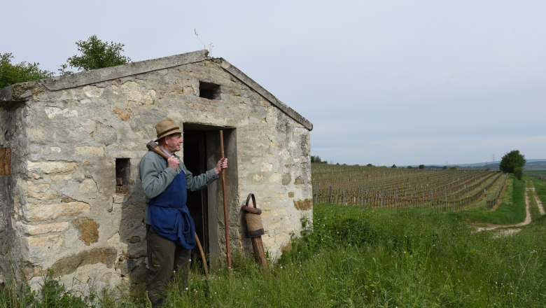 Hiatahittn in Straning, © Harald Veigl A man in a straw hat stands in front of a small stone hut in a vineyard.