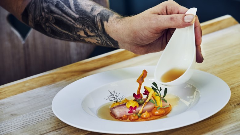 Here the eye eats with you, © Niederösterreich Werbung/Andreas Hofer A plate with artfully arranged food, over which a hand pours sauce from a small jug.