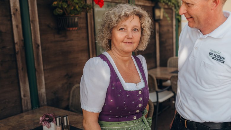 Head chef and landlady: Gabriele Engel, © Niederösterreich Werbung/Daniela Führer A woman in traditional dress stands next to a man in a white shirt with an inscription.