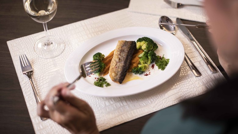 Dinner, © NMC A plate with fish fillet, broccoli and sauce, next to it a glass of white wine.