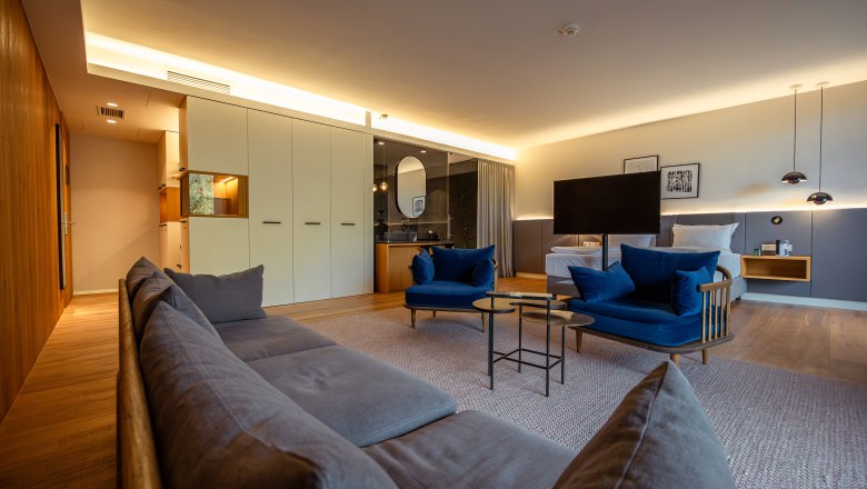 Steigenberger Hotel & Spa, Krems, © Niederösterreich Werbung/ Maximilian Pawlikowsky Modern hotel room with blue armchairs, gray sofa, large bed and stylish lighting.