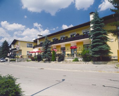 Café Restaurant Bernhart, © z.V.g. von Café Restaurant Bernhart, Foto Jürgen Bernhart Yellow building with café and restaurant, surrounded by trees, under a blue sky.
