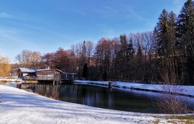 Natural pond with drinking water quality, © Wiener Alpen, intern A natural pond with clear water, surrounded by snow-covered ground and trees in the background.