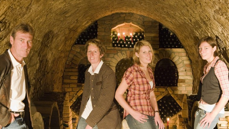 Krottendorfer family, © Michael Himml Four people in a wine cellar with brick walls and wine bottles in the background.