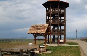 View from the Sandberg Celtic settlement with observation tower, © Keltenstadt.at Wooden observation tower on a meadow with benches and a cross in the background.