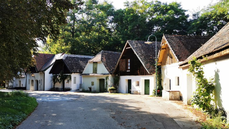 Peigarten Peregriniplatzl, © Weinstraße Weinviertel A picturesque alley with traditional white houses and sloping roofs, surrounded by trees.