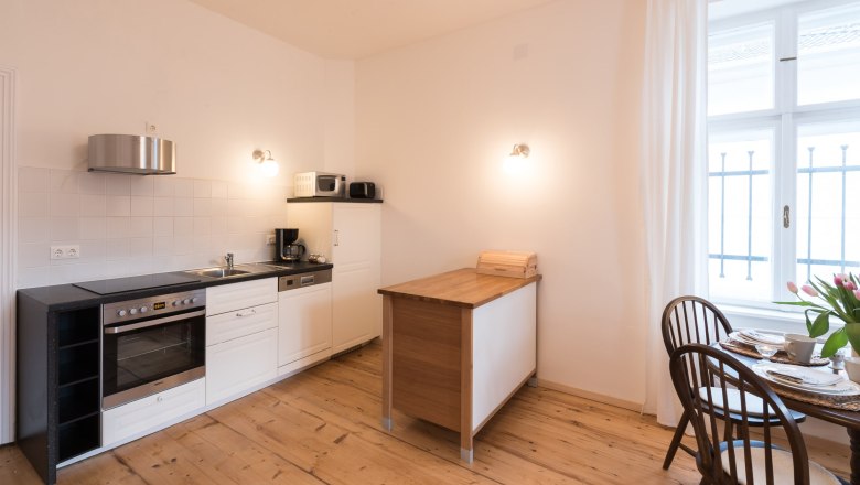 Top 2 - Kitchen, © VP FeWo OG Modern kitchen with wooden floor, white furnishings and small dining table by the window.