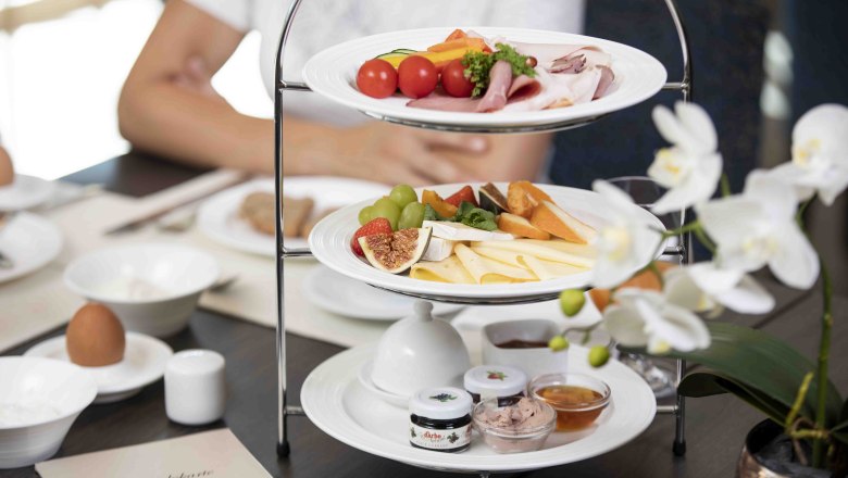 Breakfast, © NMC A breakfast table with an etagere full of cheese, cold cuts, fruit and spreads. A white orchid in the foreground.
