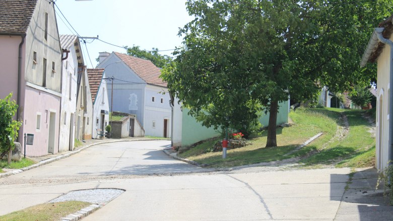 Wine cellar lane, © Gemeinde Neusiedl/ Zaya A picturesque wine cellar lane with traditional houses and a tree on a sunny day.