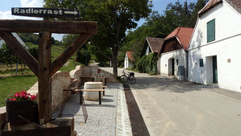 Cyclists' rest in Mailberg, © Weinstraße Weinviertel A rest area for cyclists in Mailberg with a wooden sign indicating a rest area for cyclists. Wine cellars and a bicycle can be seen in the background.