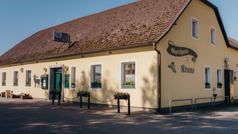 Inn with natural garden, © Niederösterreich Werbung/Daniela Führer Yellow inn with brown roof and green door, labeled 'Gasthaus Kraus'.