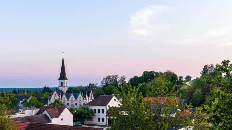 Jedenspeigen, © Gemeinde Jedenspeigen View of the Jedenspeigen church at sunset, surrounded by trees and houses.