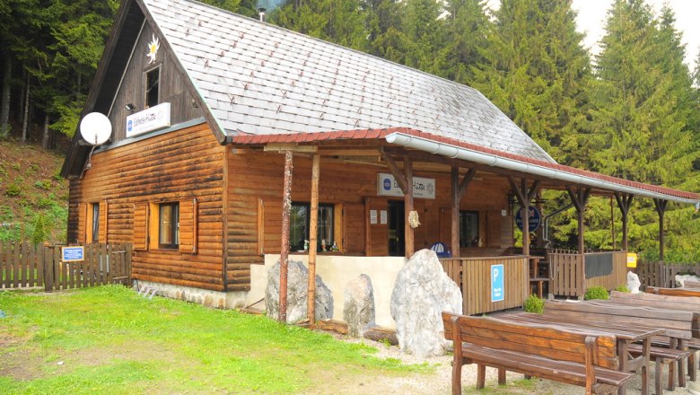 Edelweiss hut Rax, © Edelweisshütte, Foto Andrea Pazman A wooden hut in the forest with tables and benches in front of it.