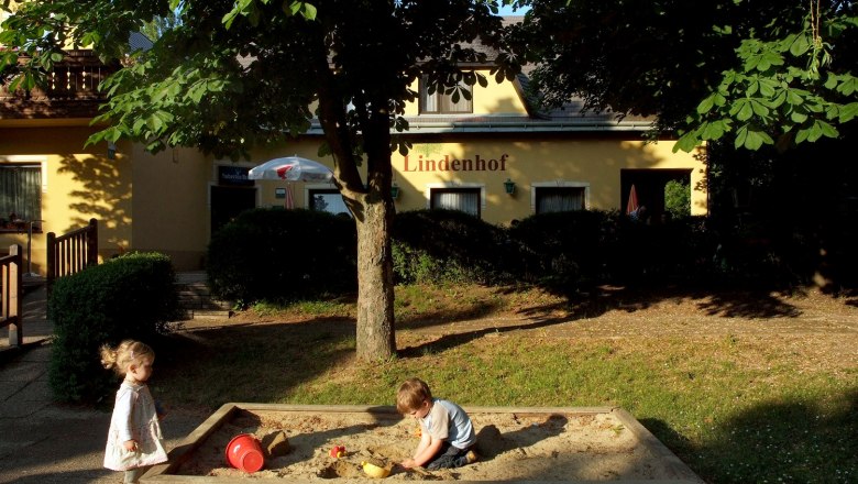 Lindenhof, © Seymannfilm Two children play in the sandpit in front of a building with the sign 'Lindenhof'.