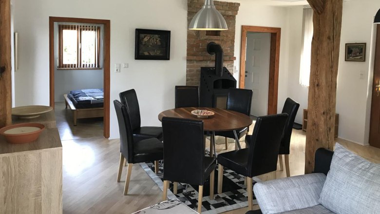 Dining area, © Familie Mokesch Dining area with round wooden table, black chairs and wood-burning stove in a room with wooden beams.