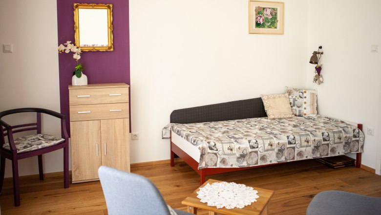 Sofa bed, © Michael Sokolar A living room with a sofa bed, a small wardrobe, a chair and a table on a wooden floor.