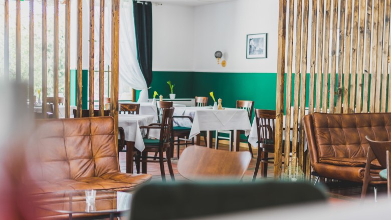 Guest room, © Schlossschenke A stylishly furnished dining room with wooden furniture, green walls and white tablecloths.