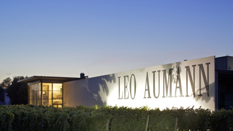 Twilight, © Weingut Aumann Building with the inscription 'Leo Aumann' at dusk, surrounded by vines.