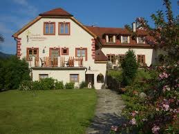 House Schneeweiss, © Birgit Schneeweiss A large, traditional house with a red roof and flowering garden in the foreground.