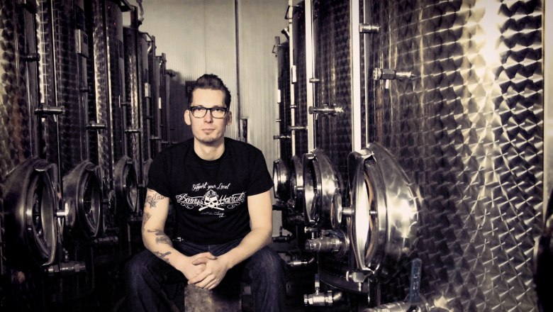 Winemaker René Pollak, © Matthias Karasek A man sits between large stainless steel tanks in a winery.