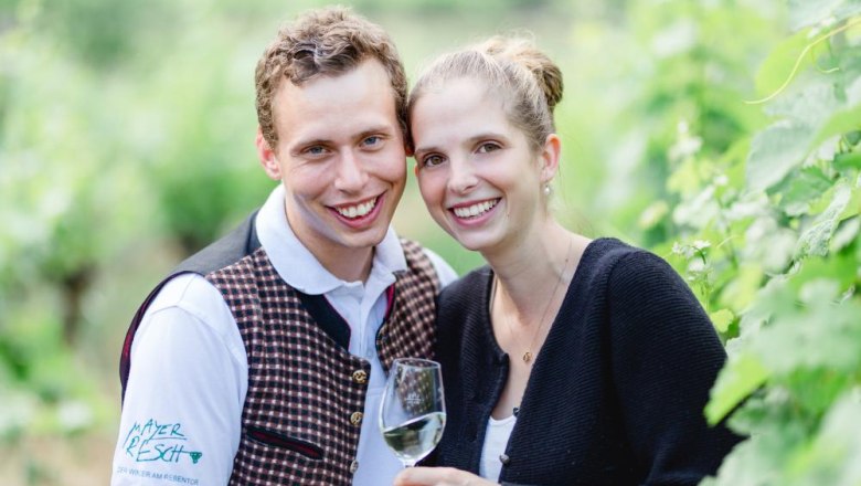 The host couple, © Alexander Pfeffel A smiling couple in a vineyard, the man wearing a vest, the woman holding a wine glass.