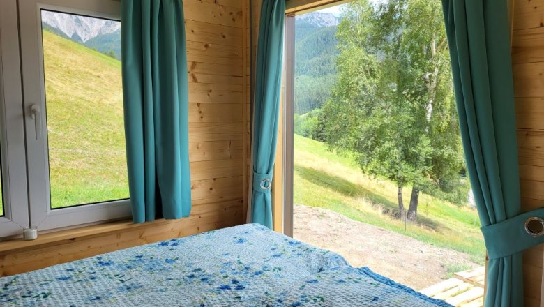 Sleeping with a view, © Villa to go Interior view of a room with a bed and large windows offering a view of a green landscape.