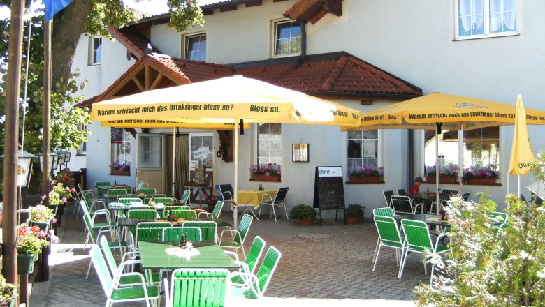 Guest garden, © Martin Zwinz A cozy garden with green tables and chairs under yellow parasols in front of a building.
