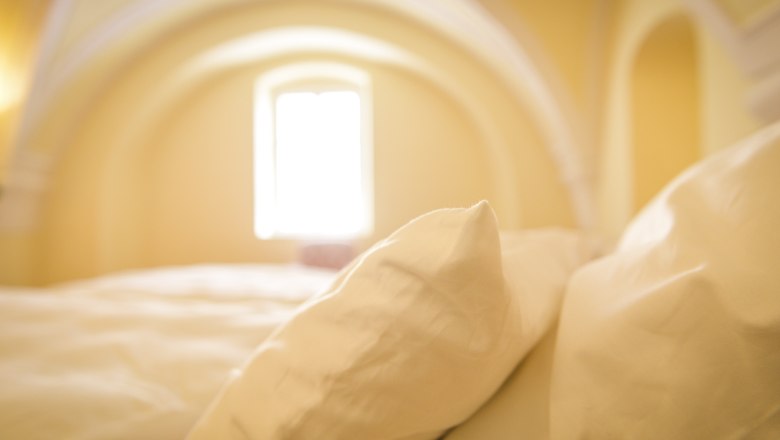 Oberstockstall Estate, © Robert Herbst Close-up of pillows on a bed in a room with a vaulted ceiling and window.