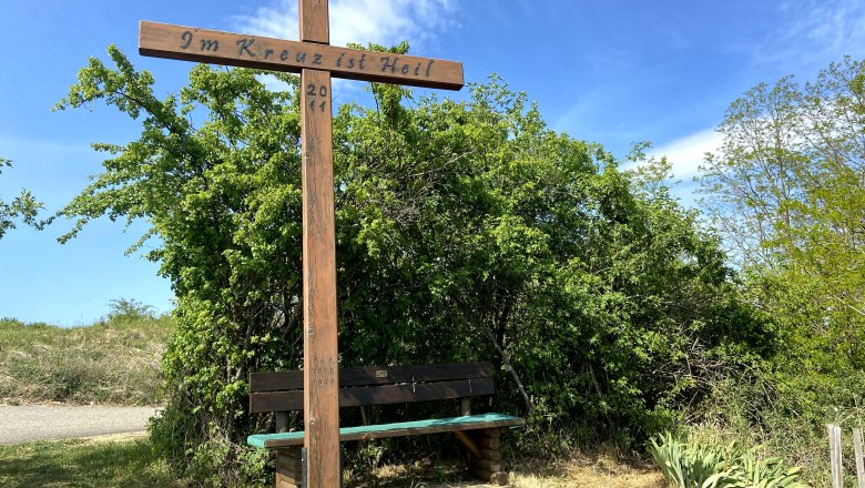 Rabl cross Oberdürnbach, © Weinstraße Weinviertel Wooden cross with inscription 'In the cross is salvation' and bench, surrounded by bushes and blue sky.