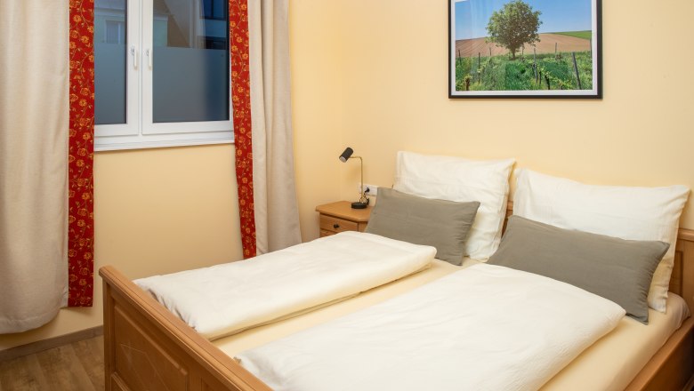 Double room, © Nadine Beles A cozy double room with a double bed, a window with curtains and a landscape painting on the wall.