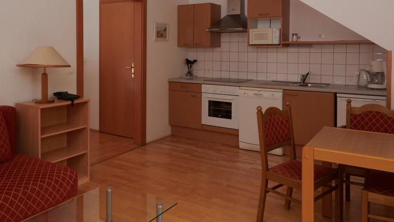 Kitchen, © Landhaus Puchbergerhof by smc Compact kitchen with wooden cupboards, dining table and chairs, stove, sink and microwave.